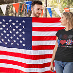 Peace Love America Sunflower 4th of July America Flag Hippie T-Shirt - Happy Patriotic 4th July Day-t-shirt-mockup-of-a-blond-woman-standing-next-to-an-american-flag